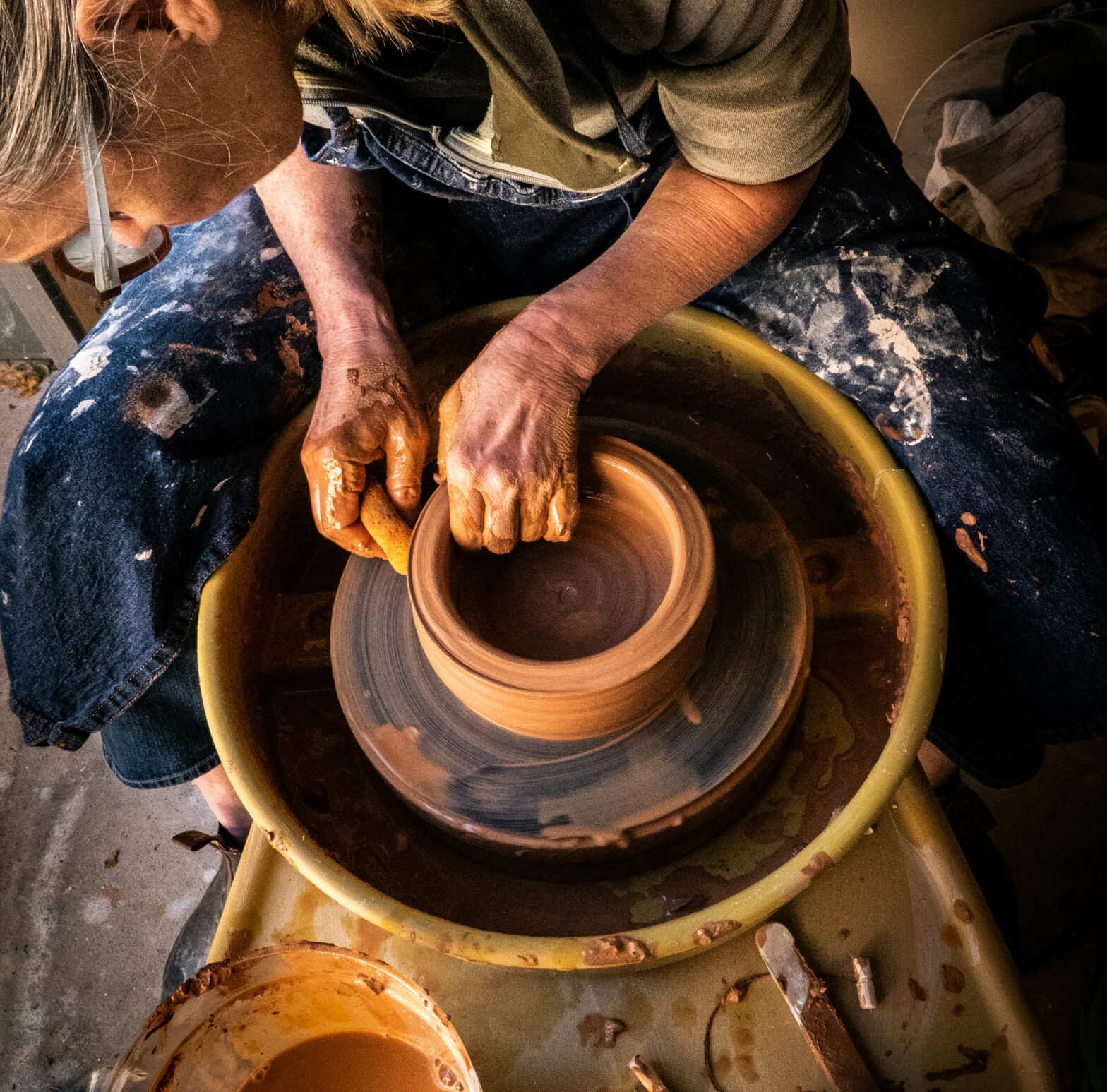 An artisan working with clay on a potter's wheel in a brightly lit studio